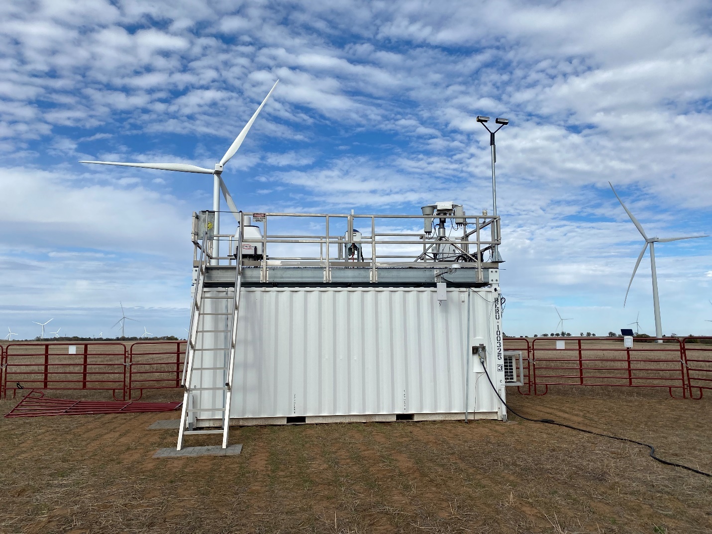 A Doppler lidar and other instruments operate on an ARM container roof with turbines behind them.