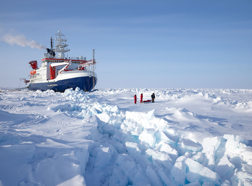 The Polarstern drifts in the arctic ice with scientists in the front on the right side.