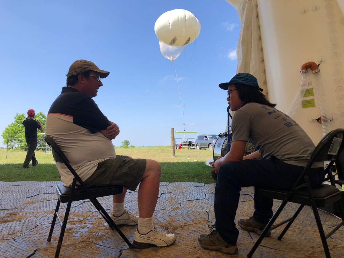 Michael Jensen and Chongai Kuang sit and talk while a tethered balloon system hovers in front of them.