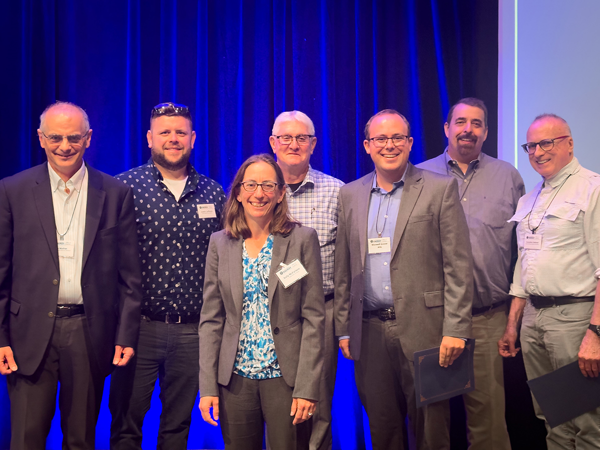 Group photo in front of a blue curtain shows, from left to right, Jim Mather, Justin LaPierre, Sally McFarlane, Fred Helsel, Max Grover, Mike Wasem, and Corydon Ireland
