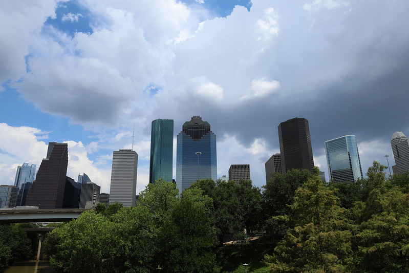 Clouds shade downtown Houston's skyline, with trees lining the foreground. Photo is by Guy Tubbs.