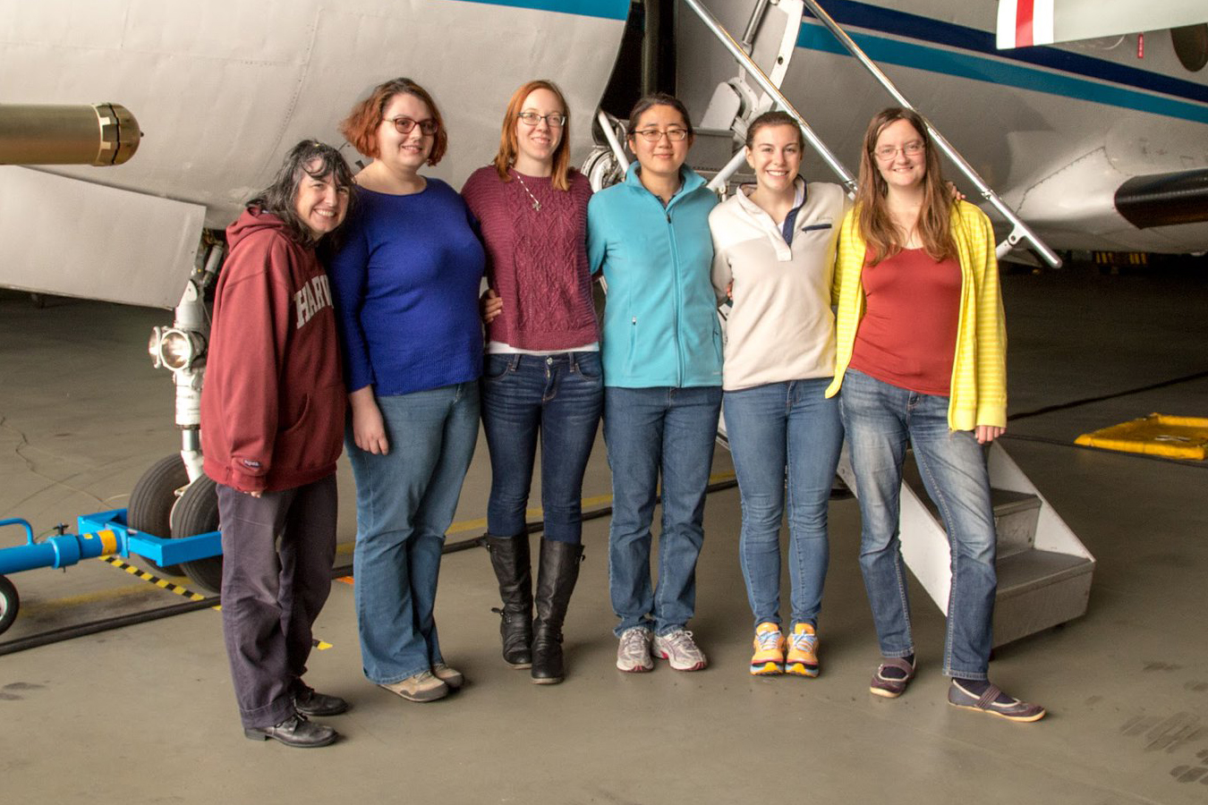 Amy Sullivan, Maria Zawadowicz, Alyssa Matthews, Fan Mei, Lexie Goldberger, and Susanne Glienke stand together in front of the stairs to the Gulfstream-159 (G-1) research aircraft.