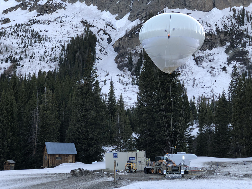 In front of a snowy backdrop, ARM's tethered balloon system hovers over the ground.