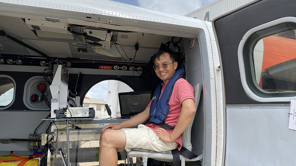 Zhien Wang sits in a Twin Otter aircraft with his head turned to smile for the camera.