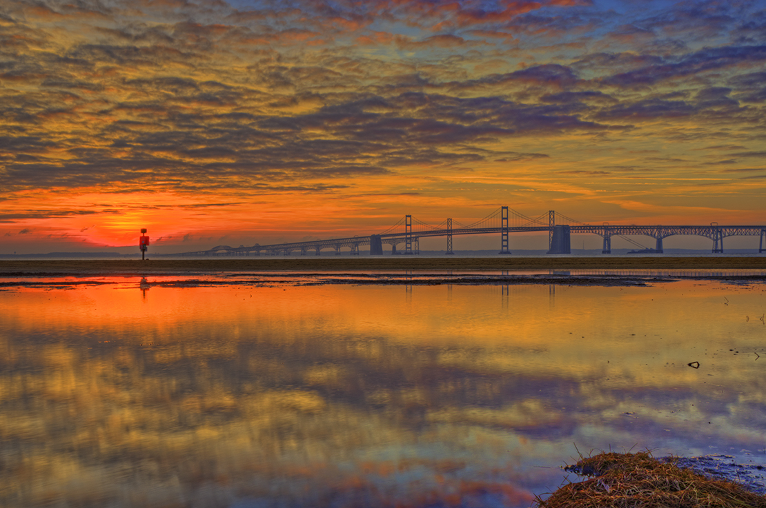 Chesapeake Bay Bridge with orange sky and clouds reflecting on the water