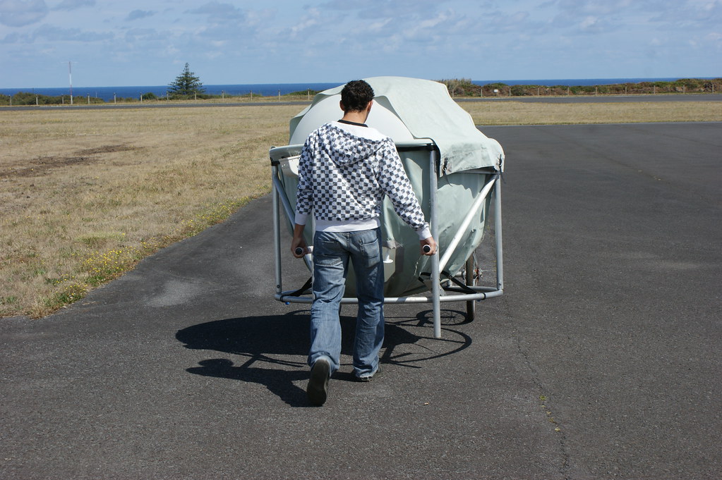 A technician wearing a black-and-white-checkered sweatshirt and jeans wheels a balloon in a cart out to the launch area.