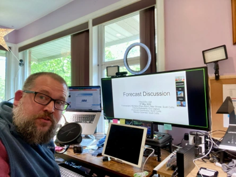 Scott Collis turns to take a picture at his desk, and his computer screen shows a slide that says, "Forecast Discussion."
