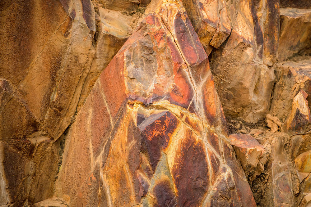 This photo provides a close-up look at an orange, yellow, and brown rock outcropping.