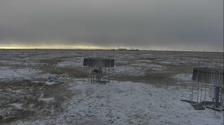 Dark, overcast sky above tundra lightly covered with snow. Two instruments stand on the tundra.