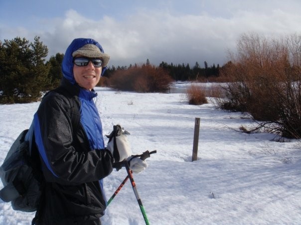 Standing on snow, Daniel Feldman smiles at the camera while holding skis.