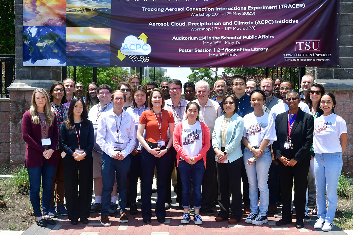 Three rows of attendees stand together under a banner that lists the TRACER and ACPC workshops and related poster session.