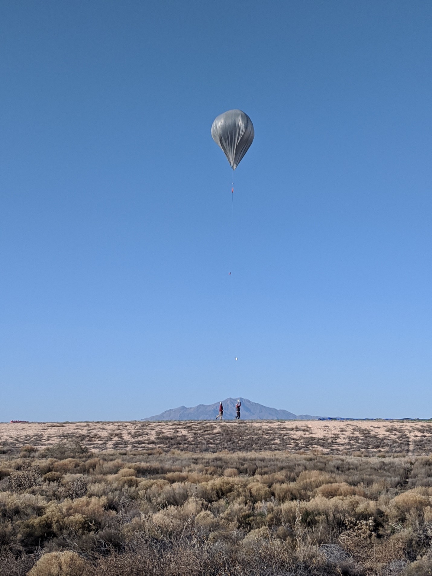 In front of a cloudless sky, a solar-powered hot air balloon floats above the desert.