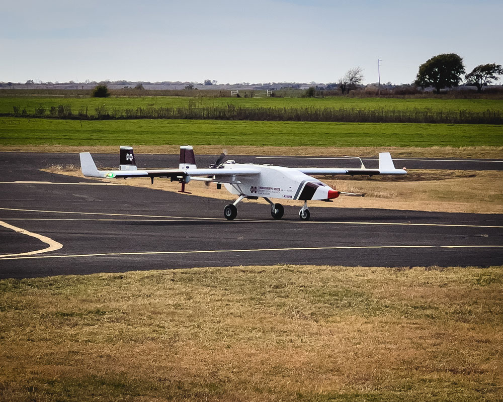 The Mississippi State University uncrewed aerial system sits on the tarmac in front of a grassy area.