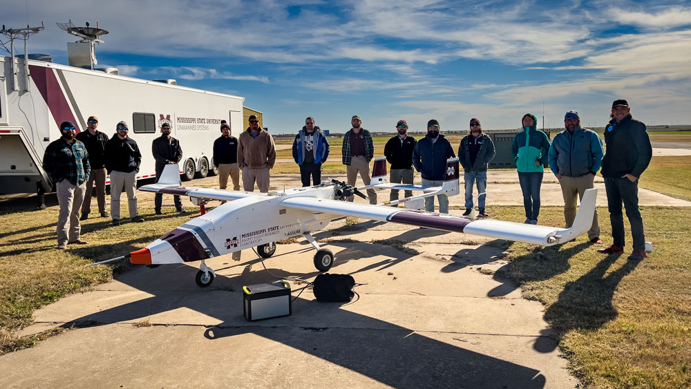 Fourteen people gather around the Mississippi State University Raspet Flight Research Laboratory's TigerShark uncrewed aerial system.