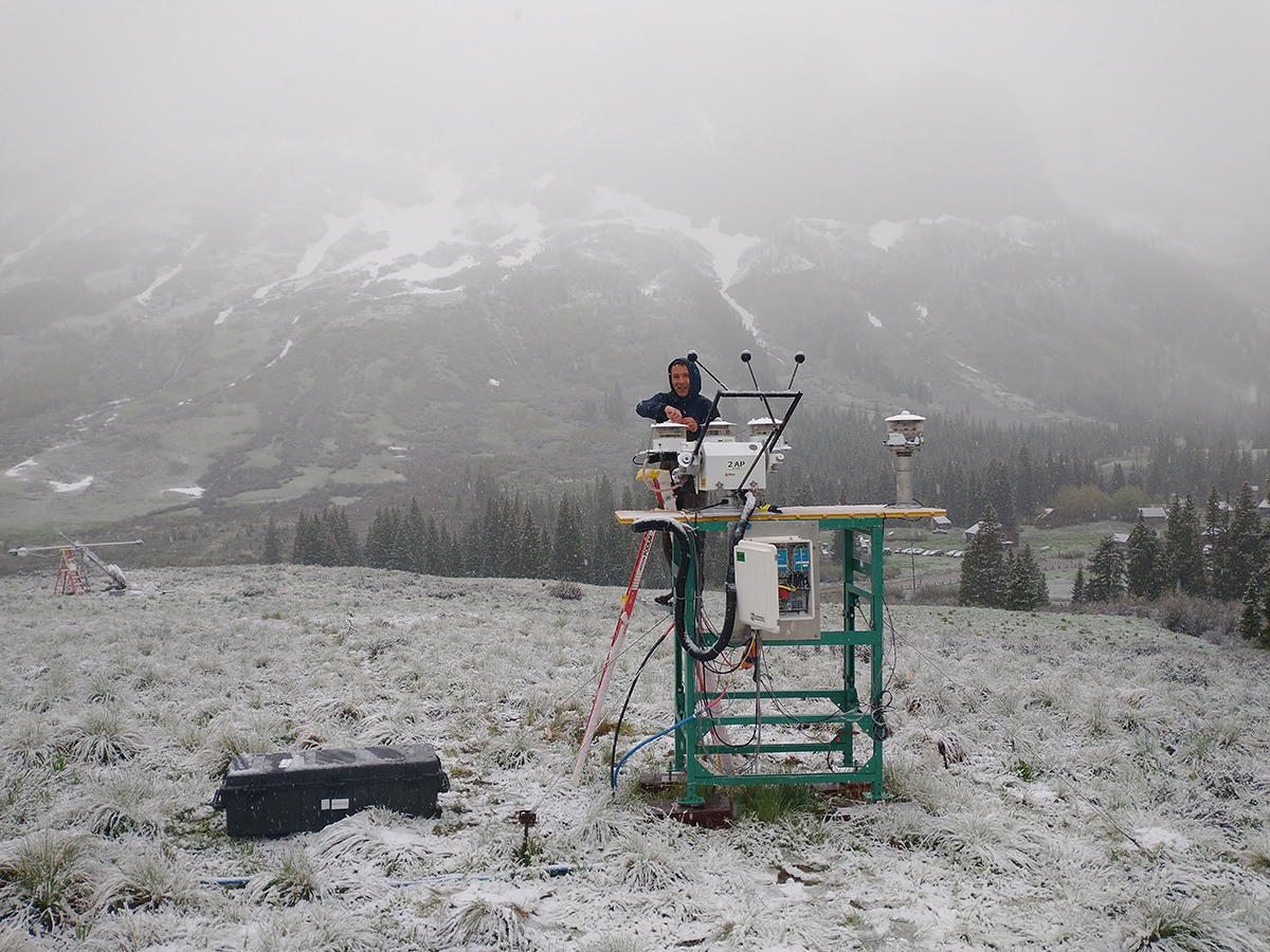 With a hood protecting his head from the elements, Bruno Cunha stands on a ladder in snow to disassemble a radiometer suite.