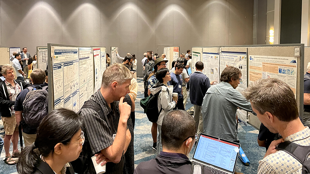 A small group looks at a laptop screen while others mill around rows of posters.