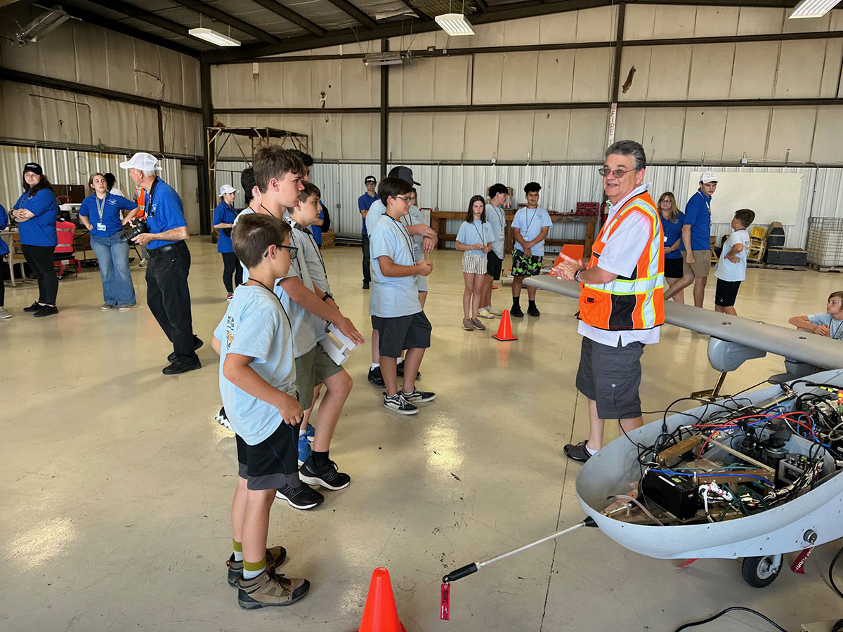 ARM Aerial Facility Manager Beat Schmid stands next to the nose of the ArcticShark while describing the uncrewed aerial system to a group of school-age children in an aircraft hangar.