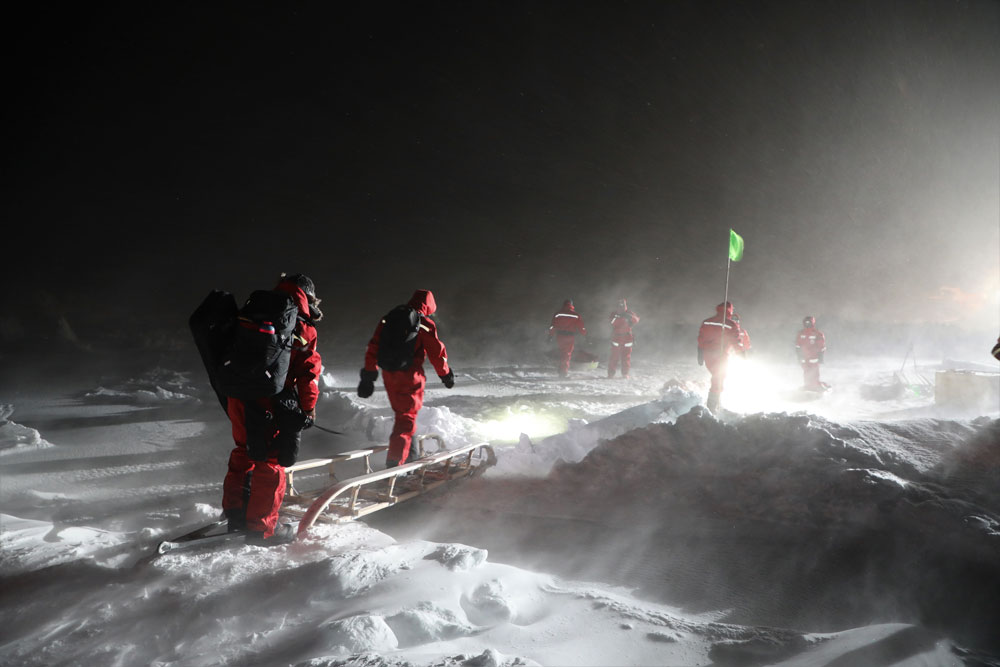 MOSAiC expedition team members use a sled as a footbridge to cross over a crack in the ice floe.