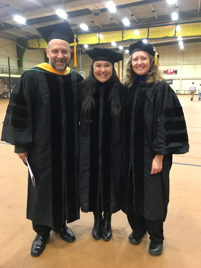 Paul DeMott, Christina McCluskey, and Sonia Kreidenweis pose in caps and gowns.
