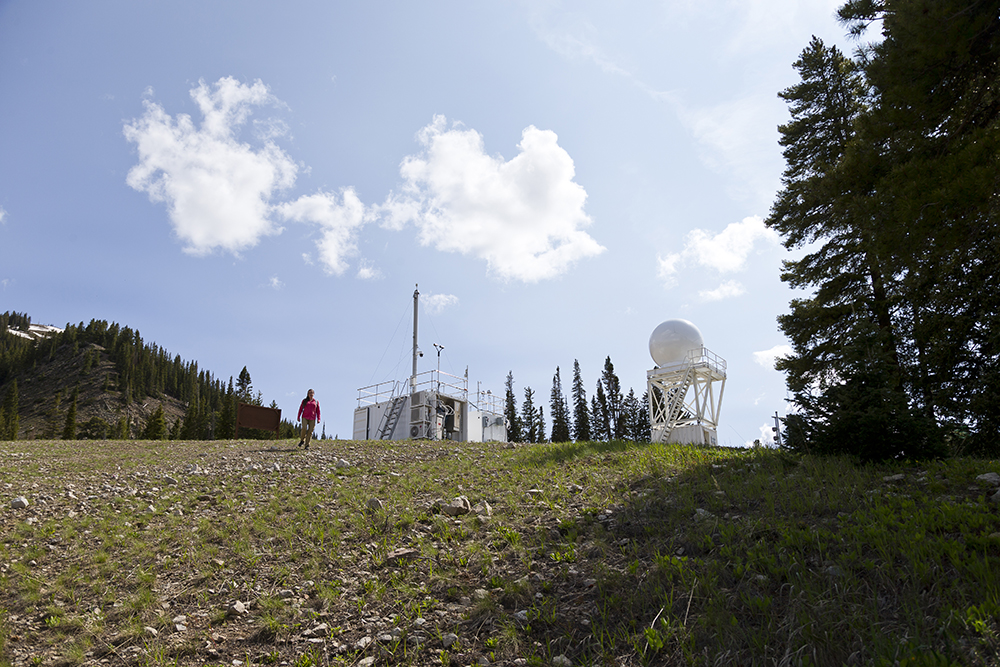 Allison Aiken walks down a hill with the Aerosol Observing System and X-band radar behind her.