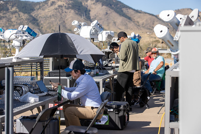 With radiometers all around, a person sits at a computer screen under an umbrella, and others are standing nearby looking down at equipment. Others are in the background observing and looking at their work.