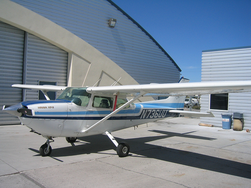 A Cessna 172 sits parked in front of its hangar.