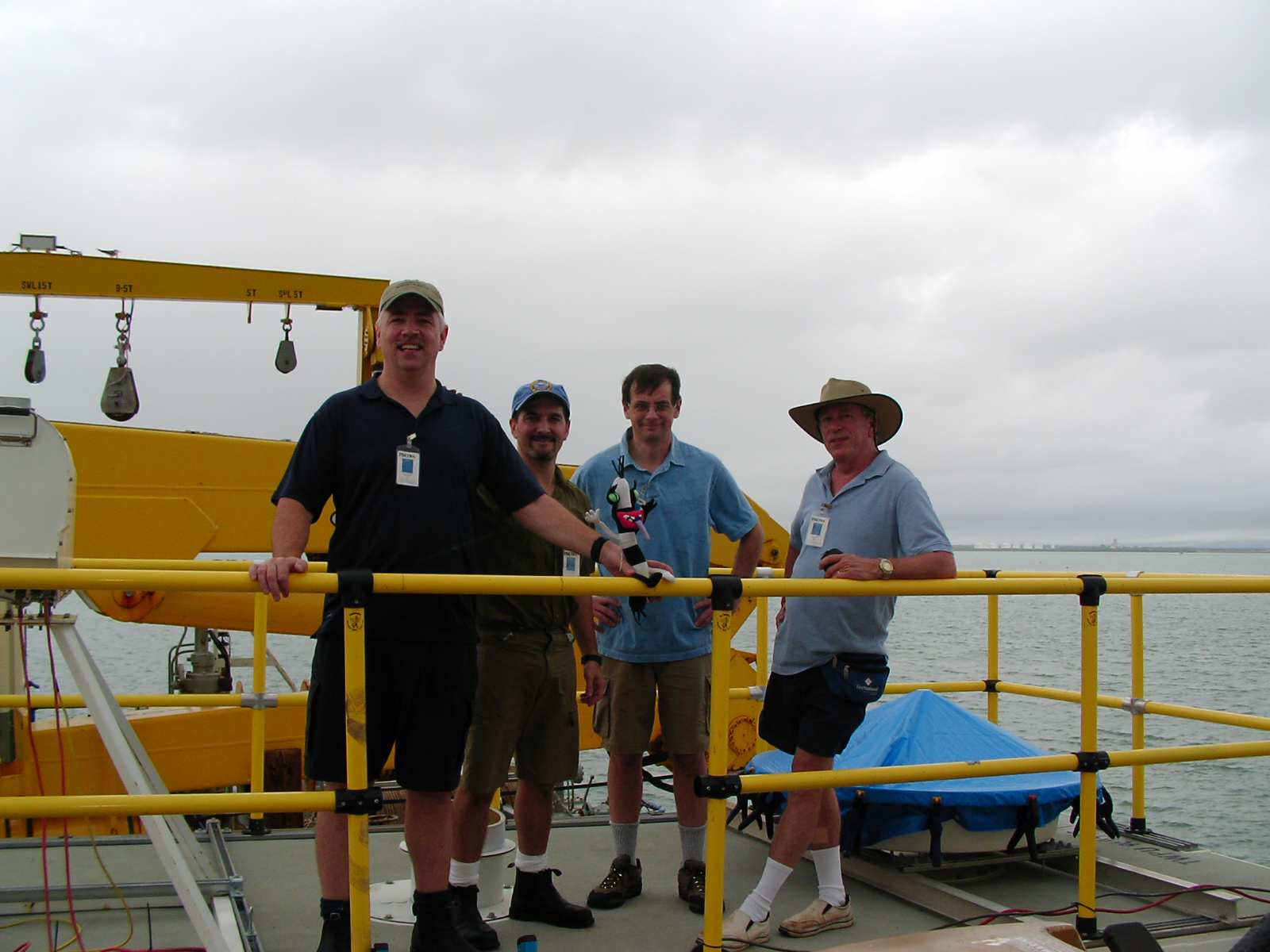 Kevin Widener, Connor Flynn, Jim Mather, and Chuck Long stand on a platform on the water. Widener is propping up PARSL Pete on a yellow railing.