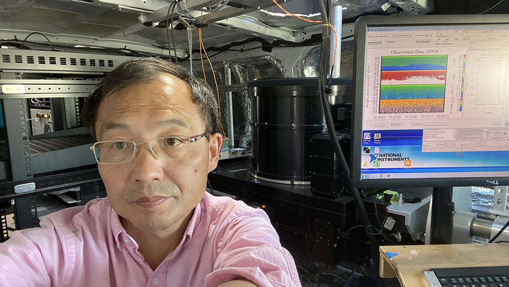 Zhien Wang sits next to a computer screen displaying data from September 28, 2023. The y-axis is labeled Height above aircraft, and the x-axis shows a time range from 21:49:53 to 22:00:23.