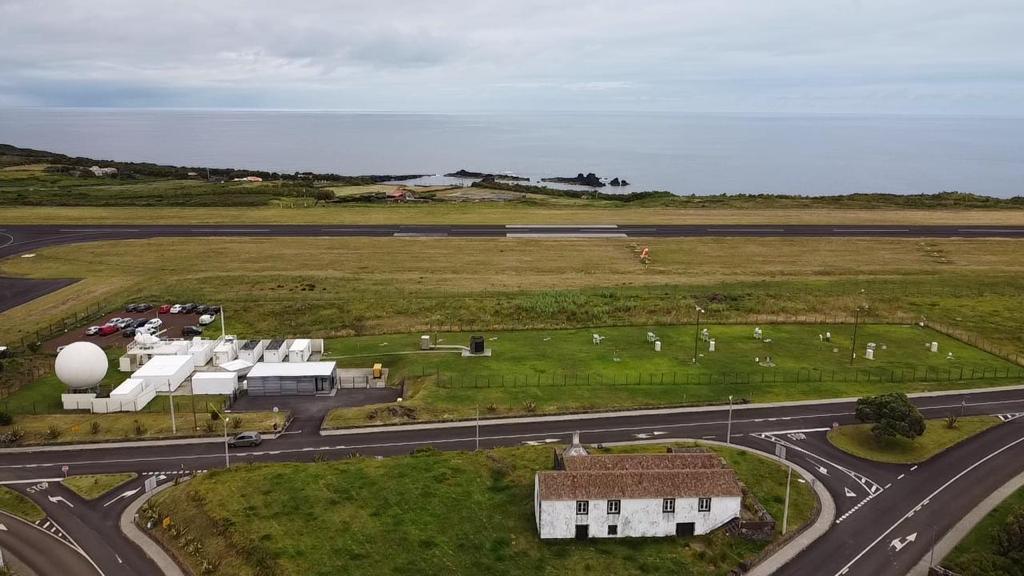 An aerial view captures the Eastern North Atlantic (ENA) observatory, including its office, radars, and full instrument field. Clouds blanket the Atlantic Ocean just beyond the ARM observatory.