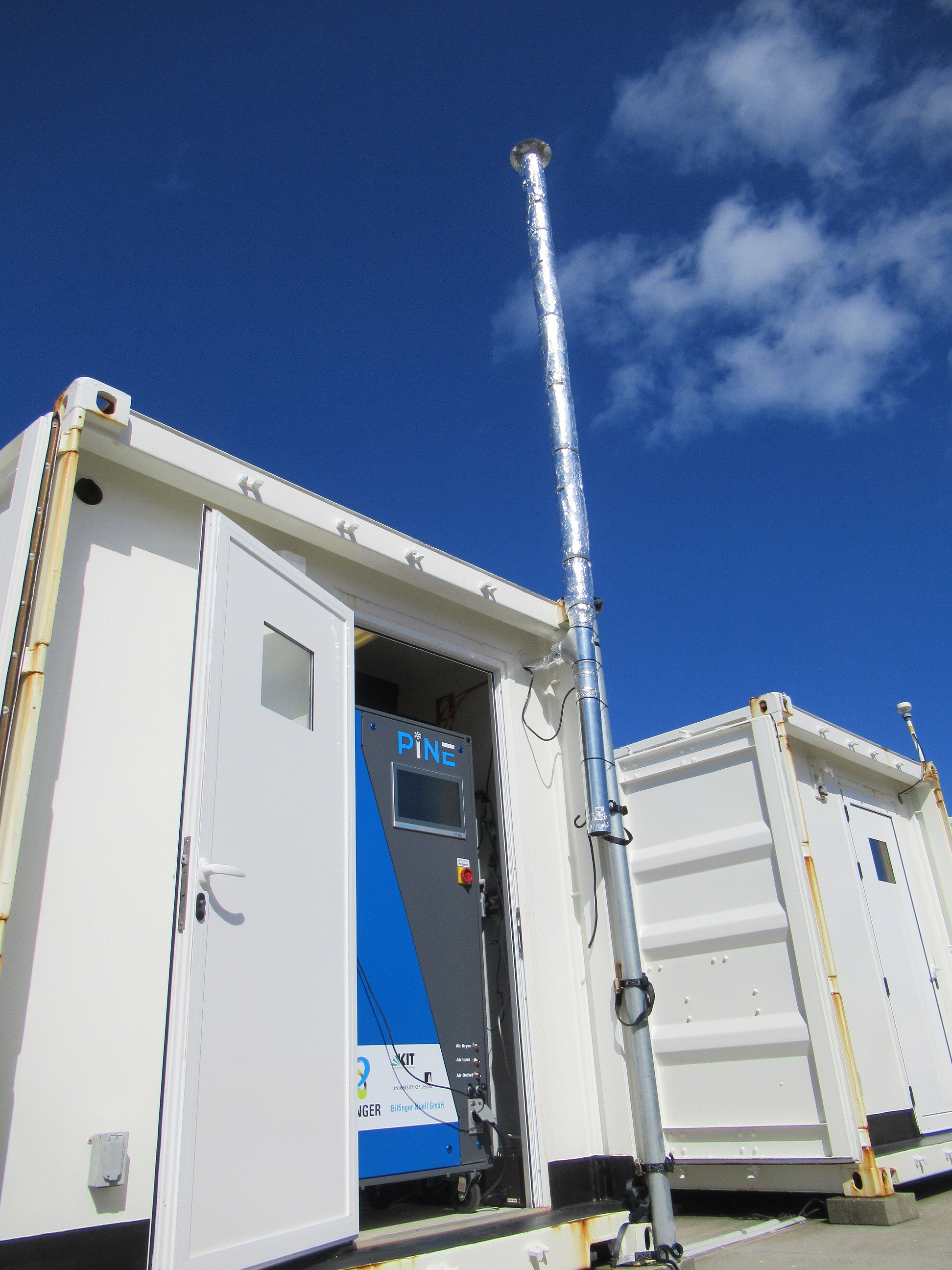The PINE chamber operates inside a container while an aerosol stack stretches from the ground up toward the sky.