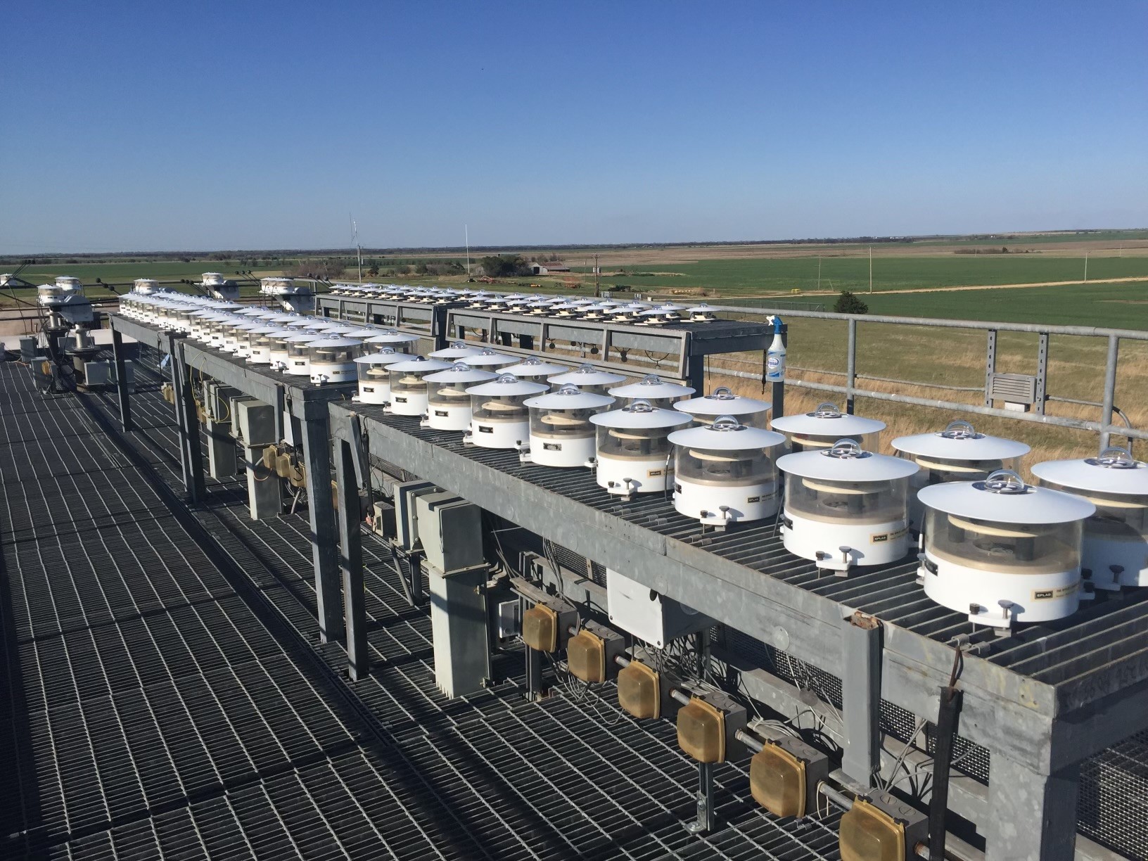 Radiometers are set up for a Broadband Outdoor Radiometer Calibration (BORCAL) session at ARM’s Southern Great Plains atmospheric observatory in Oklahoma. Pyranometers are mounted on two rows of tables. In the background, pyrgeometers are mounted on solar trackers.