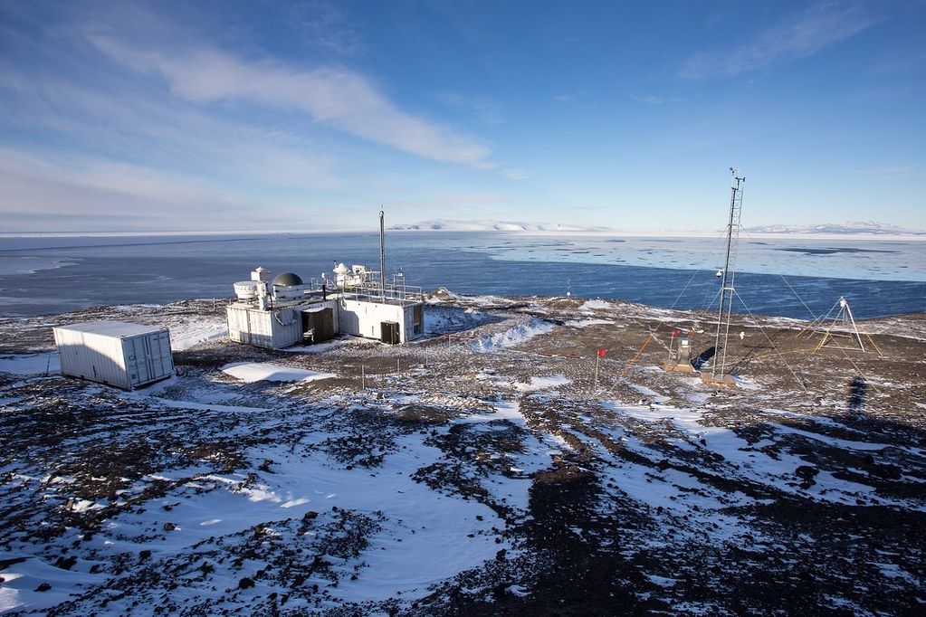 ARM radars and containers are situated on land in Antarctica with sea ice on the horizon.