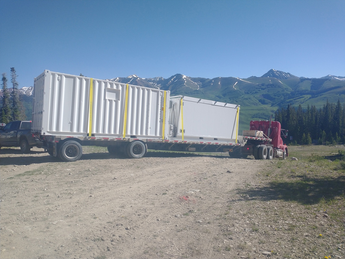 Two cargo containers are strapped down to a large truck beginning its descent down a dirt road.