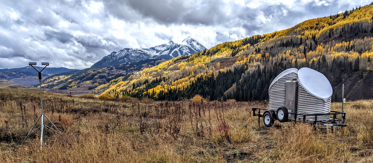 A disdrometer is distanced from a snow-level radar in a grassy area.