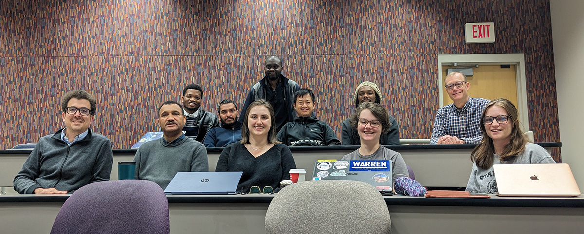 Five people sit in the front row, five sit in the back, and one is crouching slightly while standing behind them.