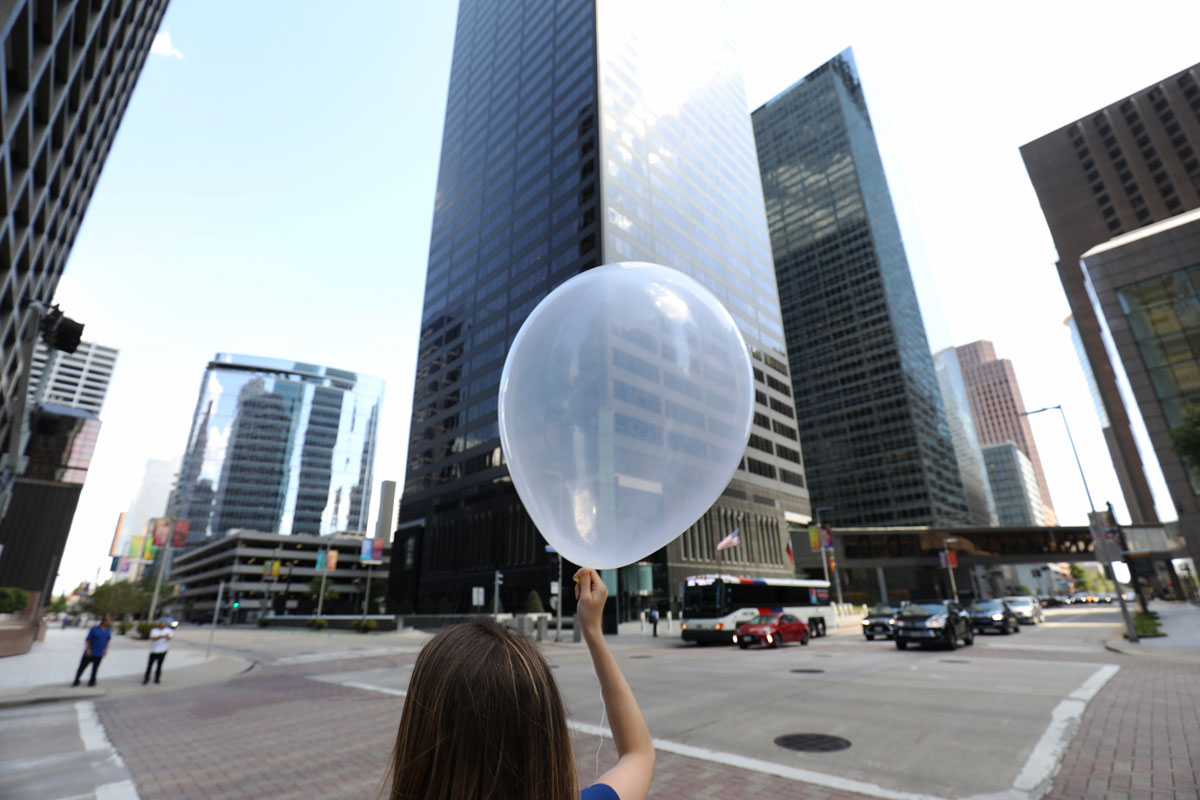 With her back to the camera, Brookhaven National Laboratory scientist Katia Lamer lifts her arm to release a mini radiosonde balloon in downtown Houston, Texas.