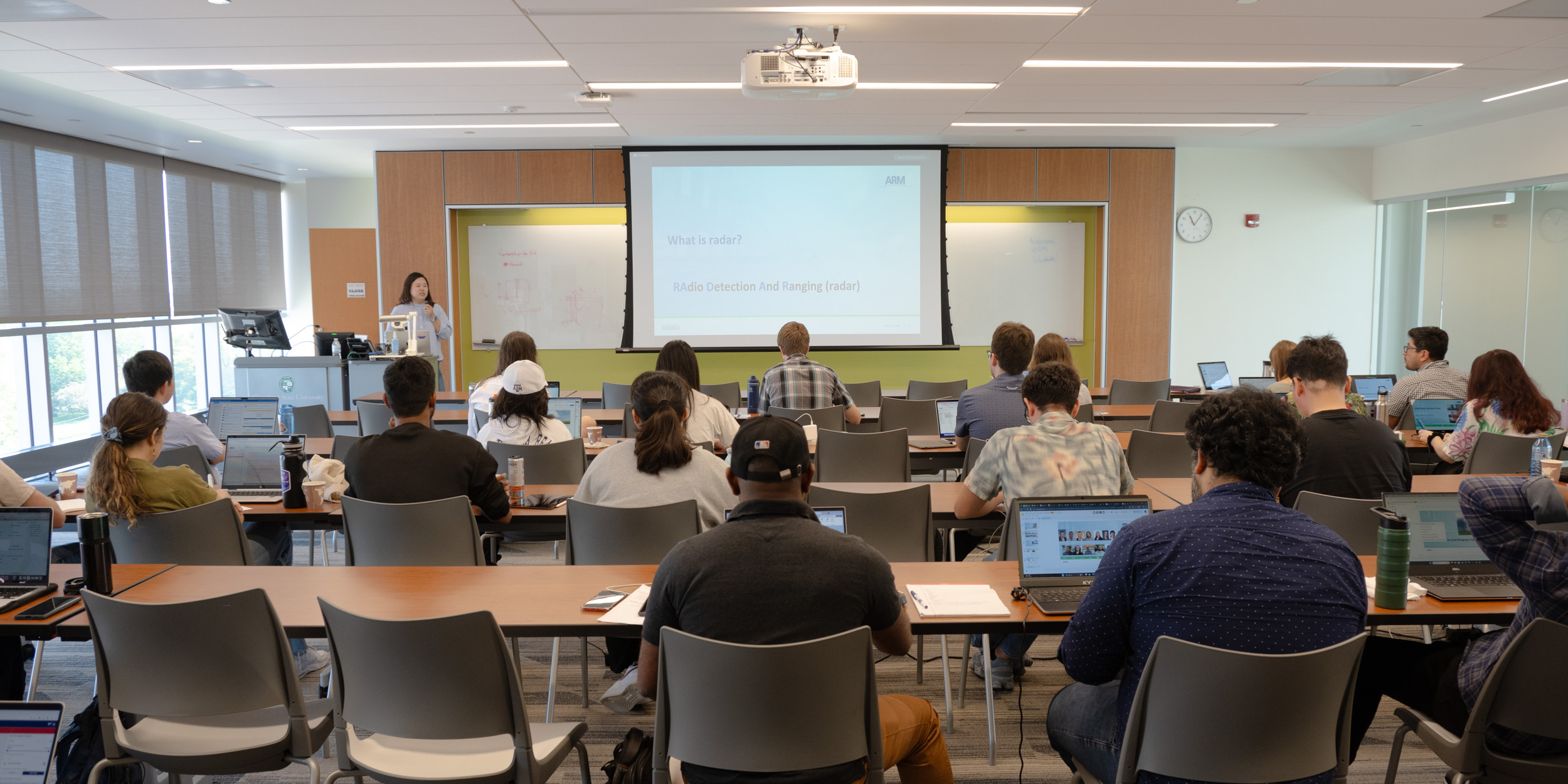 Ya-Chien Fang stands in front of rows of students sitting at tables while presenting a screen that says "What is radar?"