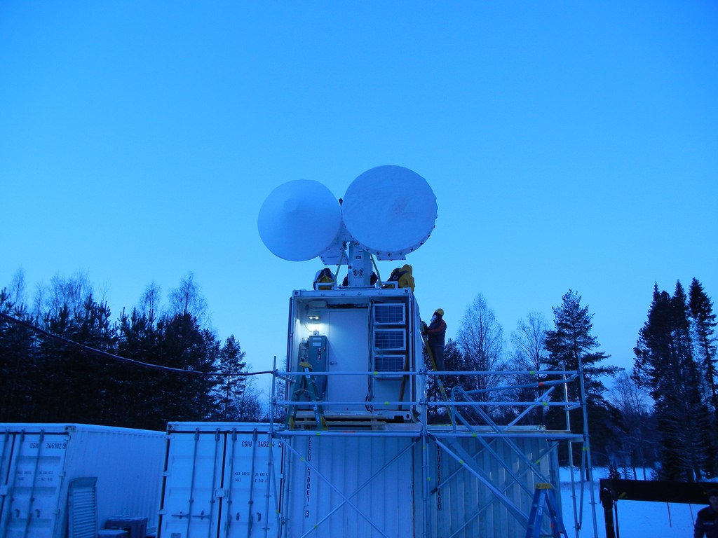 Radar engineers climb on top of an ARM Mobile Facility to install scanning ARM radars in a forested area.