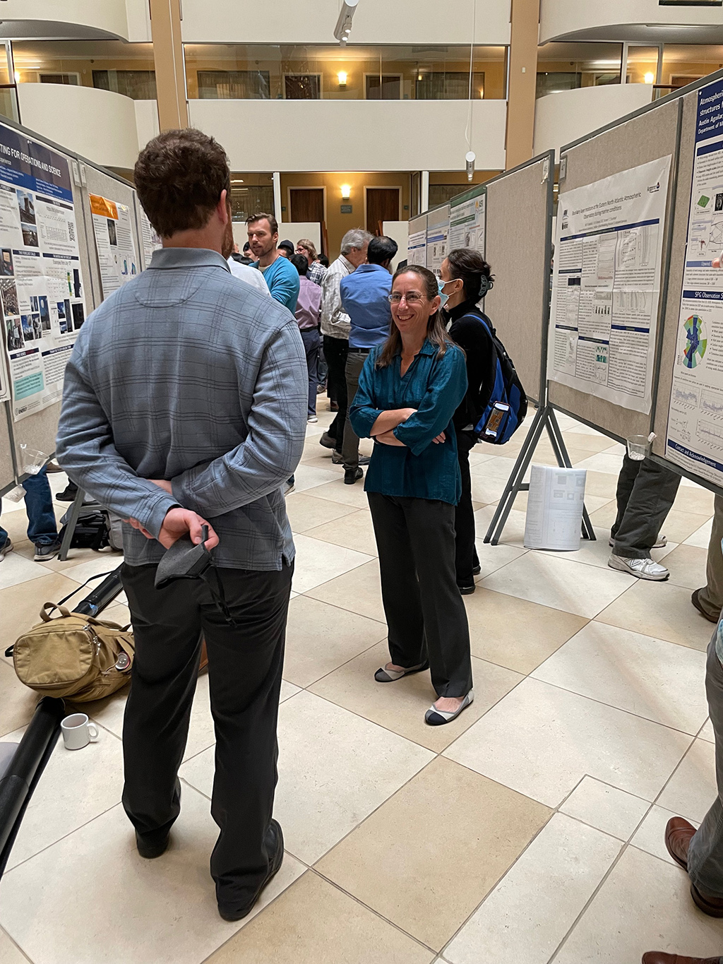 Sally McFarlane stands with her arms crossed and smiles while talking in the middle of a poster session.