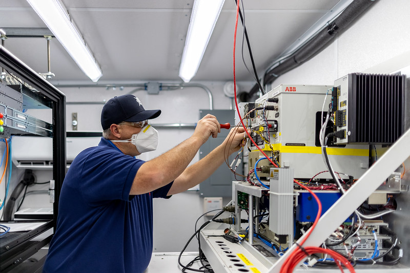 Wearing a mask, David Oaks uses a screwdriver while working on an atmospheric emitted radiance interferometer.