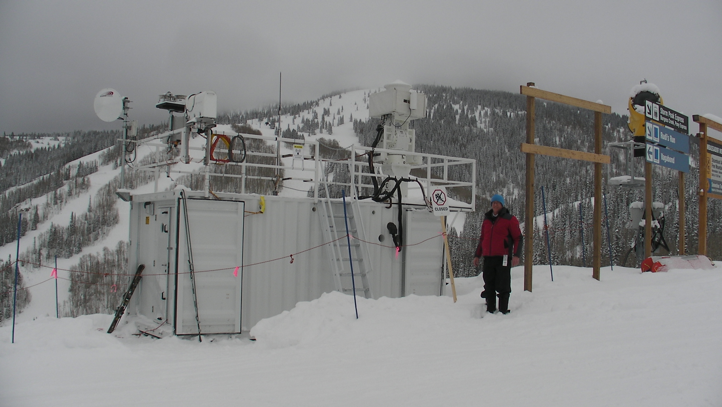 Chuck Long stands in ankle-deep snow on a cloudy day in the mountains next to an ARM operations van.