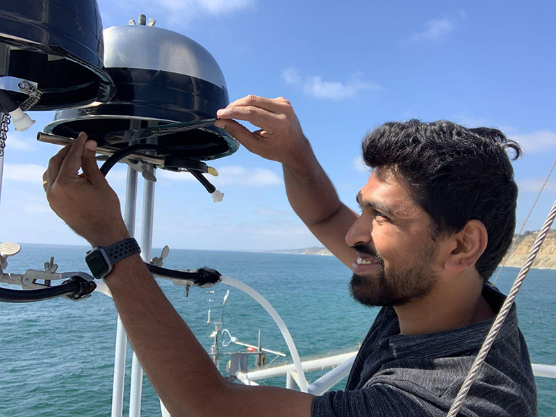 Tim Devadoss smiles as he performs work on an ice-nucleating particle collector during EPCAPE in La Jolla, California. He's working near the ocean end of Scripps Pier.