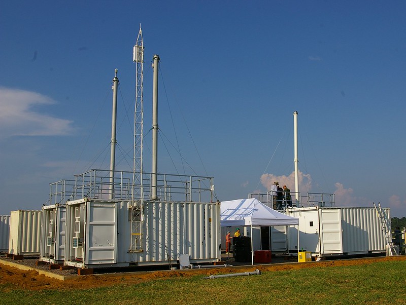 Aerosol stacks rise up from instrument containers while people work on the roof of a smaller neighboring container.