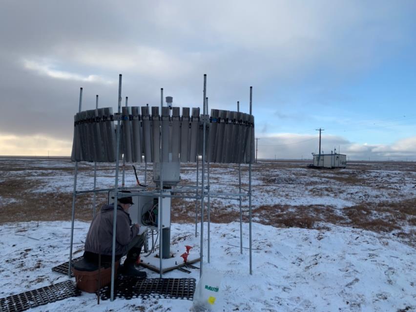 Ken Irving sits under an instrument in the snow-covered tundra.