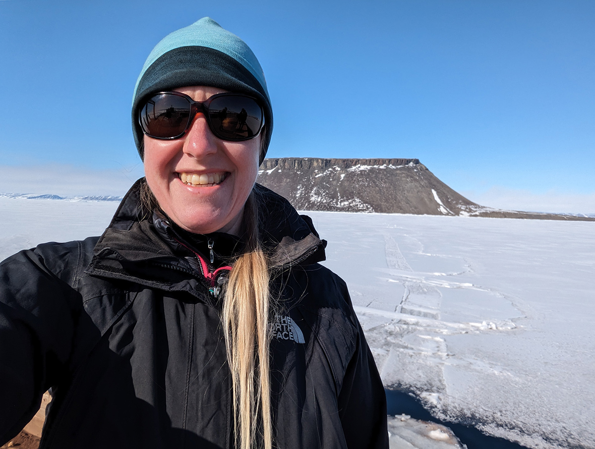 Kerri Pratt smiles in front of flat, snow-covered ground and, in the distance, a plateau sprinkled with snow.