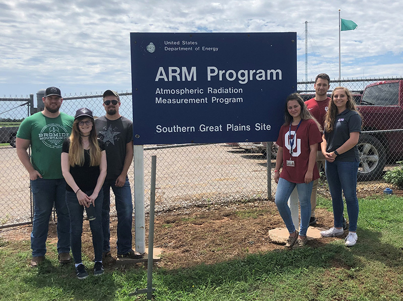 Corey Godine, Alyssa Sockol, Austin King, Madisyn Farris, Tyler Radebaugh, and Annalisa Sanfilippo flank a sign that says, "United States Department of Energy ARM Program Atmospheric Radiation Measurement Program Southern Great Plains Site."