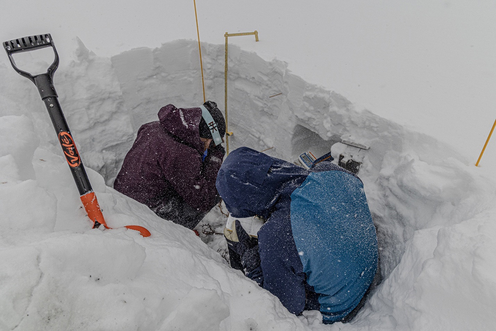 Eli Schwat and Danny Hogan sit in a snow pit and take down measurements.