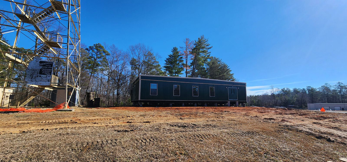 The trailer for the Bankhead National Forest atmospheric observatory's main site office is located next to a fire tower with a sign that says, "Only you can prevent forest fires."