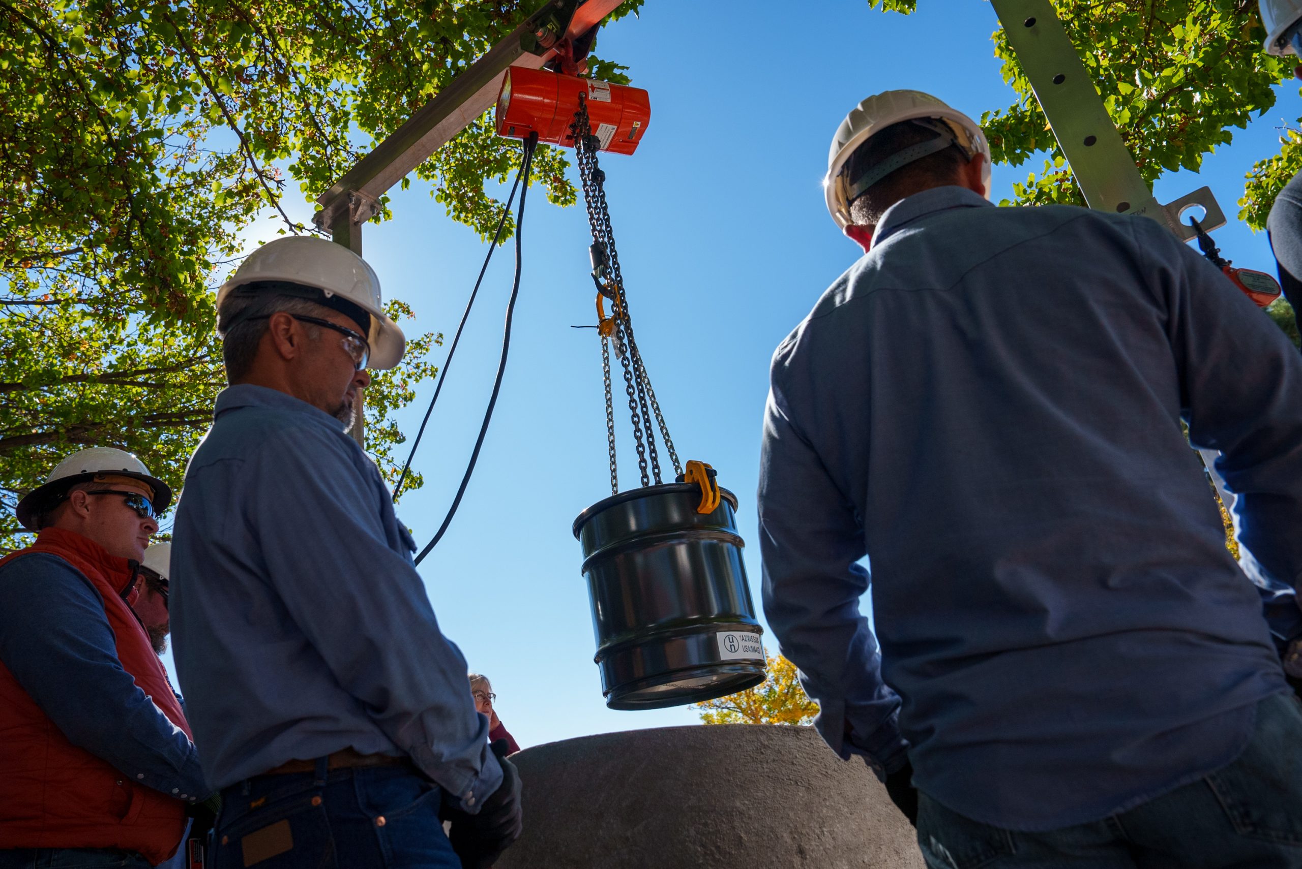 Workers look on as a metal barrel containing historical items from Sandia is lowered into the ground.